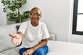 Mature hispanic woman sitting on the sofa at home smiling friendly offering handshake as greeting and welcoming Royalty Free Stock Photo