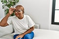 Mature hispanic woman sitting on the sofa at home very happy and smiling looking far away with hand over head Royalty Free Stock Photo