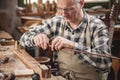 Mature instrument maker inside a rustic workshop is winding a wire around a violin bow