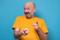 Mature joyous man in yellow casual shirt pointing at camera and laughing