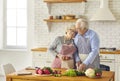 Mature loving couple in cooking aprons hugging and cooking healthy vegetarian diet dish