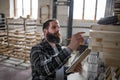 Mature male carpenter checking inventory indoors in carpentery workshop. Small business concept.