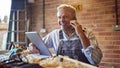 Mature Male Carpenter In Garage Workshop With Digital Tablet Talking On Mobile Phone Royalty Free Stock Photo