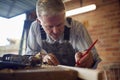 Mature Male Carpenter In Garage Workshop Marking Wood With Pencil Royalty Free Stock Photo