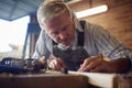 Mature Male Carpenter In Garage Workshop Planing Piece Of Wood Royalty Free Stock Photo