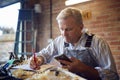 Mature Male Carpenter In Garage Workshop Working On Design Holding Mobile Phone Royalty Free Stock Photo