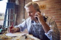 Mature Male Carpenter In Garage Workshop Working On Design And Talking On Mobile Phone Royalty Free Stock Photo