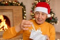 Mature male celebrating christmas at home, opening present box with ribbon, being surprised, being photographed in living room Royalty Free Stock Photo