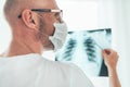Mature Male doctor portrait examining the patient chest x-ray film lungs scan at radiology department in hospital.Covid-19 scan Royalty Free Stock Photo