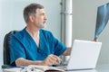 Mature male doctor working on laptop computer, sitting in medical office. Royalty Free Stock Photo