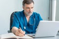 Mature male doctor working on laptop computer, sitting in medical office. Royalty Free Stock Photo