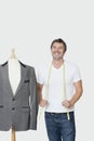 Mature male dressmaker standing next to tailor's dummy over gray background