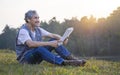 mature male with grey hair smiling and sitting at the forest park on summer