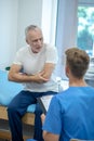 Mature male patient showing painful elbow to brown-haired doctor Royalty Free Stock Photo