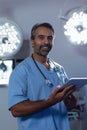 Mature male surgeon looking at camera while using digital tablet in operation room at hospital Royalty Free Stock Photo