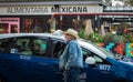 Mature male taxi driver near the car. Man with hat leaning at taxi car parked on a busy city street