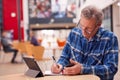 Mature Male Teacher Or Student With Digital Tablet And Mobile Phone Working At Table In College Hall Royalty Free Stock Photo