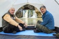 Mature male tourists sit in a tent and admire the beautiful Atysh waterfall