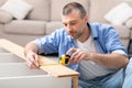 Mature Man Assembling Shelf Measuring It With Tape At Home Royalty Free Stock Photo