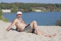 Mature man in a baseball cap and bathing shorts lying on a sandy