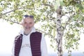 A mature man with a beard and glasses on his forehead stands under a birch tree Royalty Free Stock Photo