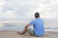 Mature man in blue t-shirt sitting on a beach looking at the sea Royalty Free Stock Photo