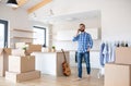 Mature man with boxes moving in new house, using smartphone.