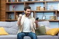 Mature man celebrating victory and successful achievement, got news online message on app using phone sitting on sofa in Royalty Free Stock Photo