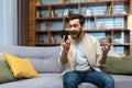 Mature man celebrating victory and successful achievement, got news online message on app using phone sitting on sofa in Royalty Free Stock Photo