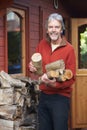 Mature Man Collecting Logs For Fire From Woodpile In Garden