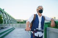 Mature man commuter with face mask and electric scooter outdoors in city, coronavirus concept. Royalty Free Stock Photo