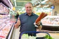 Mature man diligently choosing tasty sausage in supermarket