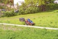 Mature man driving grass cutter in a sunny dGardener driving a riding lawn mower in a gardenay.Worker mowing grass in city park. Royalty Free Stock Photo