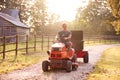 Mature Man Driving Ride On Mower Along Garden Path