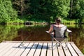 Mature man fishing from wooden pier in summer. Nearby lies a fishing rod Royalty Free Stock Photo