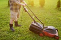 Mature man gardener cutting grass in his backyard with lawn mower on summer sunny day. Lawnmower machine for trimming grass. Royalty Free Stock Photo