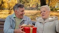 Mature man gives gift to beloved wife on birthday elderly woman happily laughs positive married couple celebrating Royalty Free Stock Photo