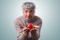 A mature man with gray hair and green eyes wearing casual sweater holding red delicious apple in his hands having surprised expres Royalty Free Stock Photo