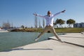 Mature man, gray-haired, with beard, sunglasses, white shirt and light brown pants, jumping in the air happy, by a lake. Concept Royalty Free Stock Photo