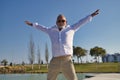 Mature man, gray-haired, with beard, sunglasses, white shirt and light brown pants, jumping in the air happy, by a lake. Concept Royalty Free Stock Photo