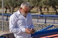 Mature man, gray-haired, bearded, sunglasses, white shirt, checking social networks on his cell phone, leaning on a railing