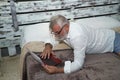 Mature man, gray-haired and bearded, wearing glasses, in pajamas, lying in bed with his laptop. Concept loneliness, retirement,