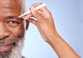 Fine, Im ready. a mature man having his eyebrow tweezed by an unrecognizable woman against a blue background. Royalty Free Stock Photo