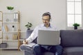 Mature man in headset with laptop working in his home office making notes sitting on couch. Royalty Free Stock Photo