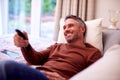 Mature Man At Home Relaxing On Sofa Watching TV Using Remote Control Royalty Free Stock Photo