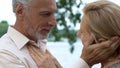 Mature man looking with love and tenderness, caring woman buttoning his shirt