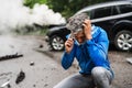 Mature man making a phone call after a car accident, smoke in the background. Royalty Free Stock Photo