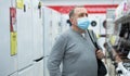 Mature man in mask choosing gas stove in appliance store