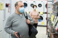 Mature man in mask choosing gas stove in appliance store