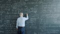 Mature man physicist writing formulas on blackboard with chalk indoors